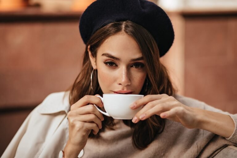 lifestyle-portrait-elegant-young-woman-with-dark-wavy-hairstyle-trendy-makeup-fashionable-beige-pullover-coat-sitting-cafe-terrace-drinking-coffee-from-white-cup (1)